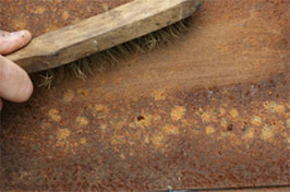 A wire brush is used to remove loose rust